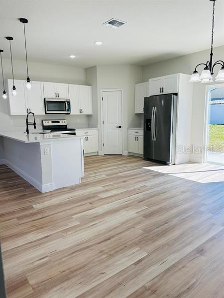 kitchen with stainless steel appliances, hanging light fixtures, light countertops, and white cabinets