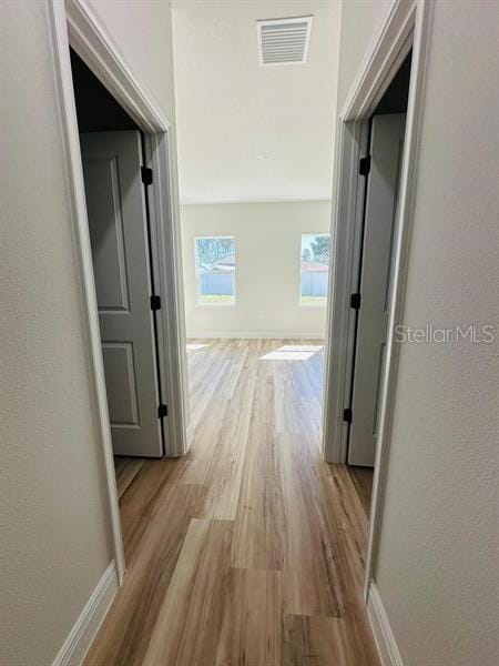 hall featuring light wood-type flooring, visible vents, a textured wall, and baseboards