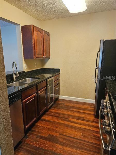 kitchen featuring baseboards, dark wood-type flooring, stainless steel appliances, a textured ceiling, and a sink