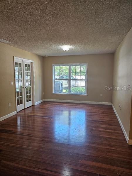 empty room with dark wood-style floors, baseboards, a textured ceiling, and french doors