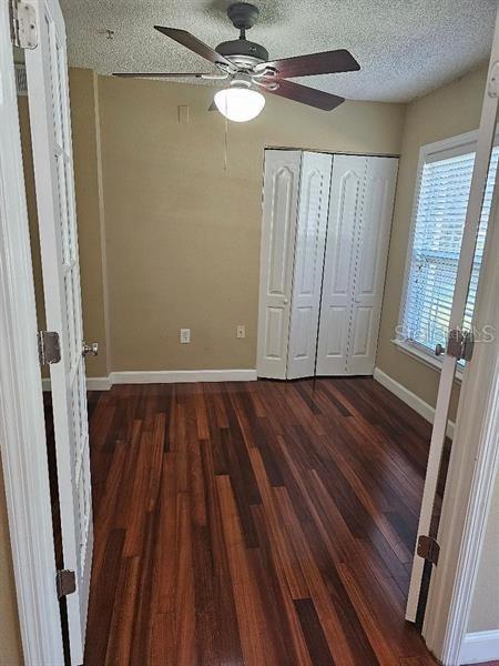 2019 Dixie Belle Dr Unit 2019O, Orlando, FL 32812 - unfurnished bedroom with baseboards, ceiling fan, dark wood-style flooring, a textured ceiling, and a closet