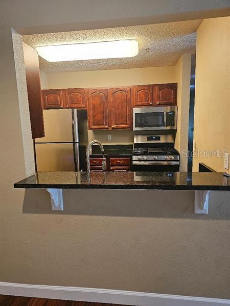 2019 Dixie Belle Dr Unit 2019O, Orlando, FL 32812 - kitchen with baseboards, dark stone counters, appliances with stainless steel finishes, a kitchen breakfast bar, and a peninsula