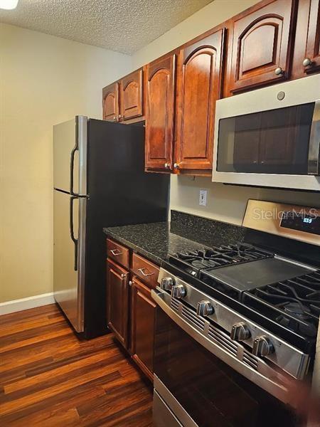 2019 Dixie Belle Dr Unit 2019O, Orlando, FL 32812 - kitchen featuring baseboards, dark stone countertops, dark wood-style flooring, stainless steel appliances, and a textured ceiling