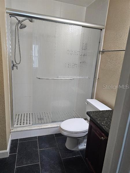 2019 Dixie Belle Dr Unit 2019O, Orlando, FL 32812 - bathroom with a textured wall, toilet, a stall shower, vanity, and tile patterned floors