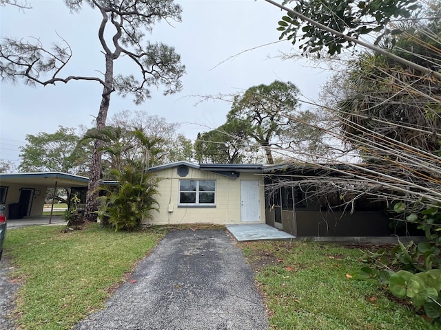 view of front facade featuring driveway, concrete block siding, an attached carport, and a front yard