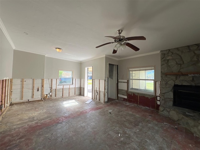 unfurnished living room featuring a wealth of natural light, crown molding, a stone fireplace, and ceiling fan