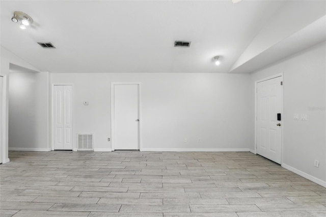 spare room with light wood-style floors, visible vents, and vaulted ceiling