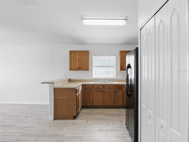 kitchen with brown cabinetry, freestanding refrigerator, a sink, and a peninsula