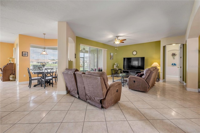 living room featuring ceiling fan, a textured ceiling, baseboards, and light tile patterned floors