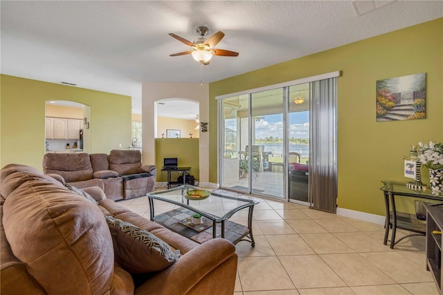 living area featuring arched walkways, light tile patterned floors, ceiling fan, a textured ceiling, and baseboards