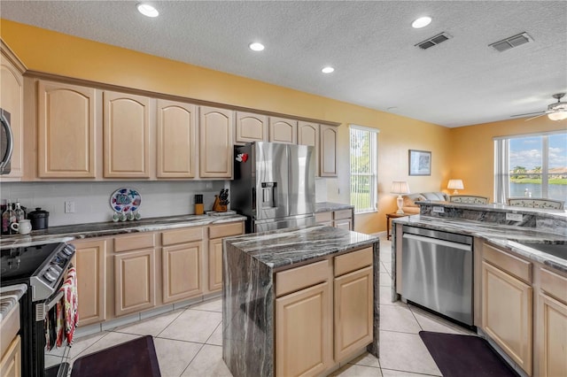 kitchen featuring plenty of natural light, visible vents, dark stone counters, stainless steel appliances, and light brown cabinetry