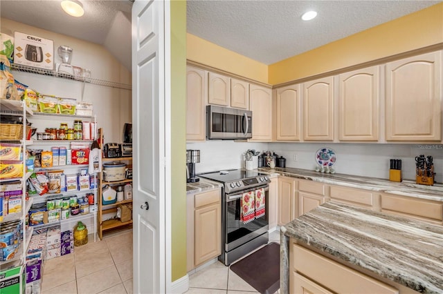 kitchen featuring stainless steel appliances, light tile patterned flooring, a textured ceiling, and light stone counters