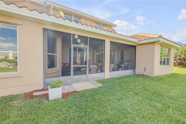 rear view of property featuring stucco siding, a tile roof, a sunroom, and a yard