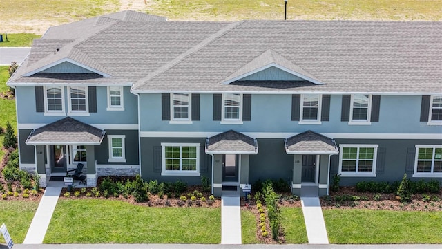 view of front of house with roof with shingles, a front yard, and stucco siding