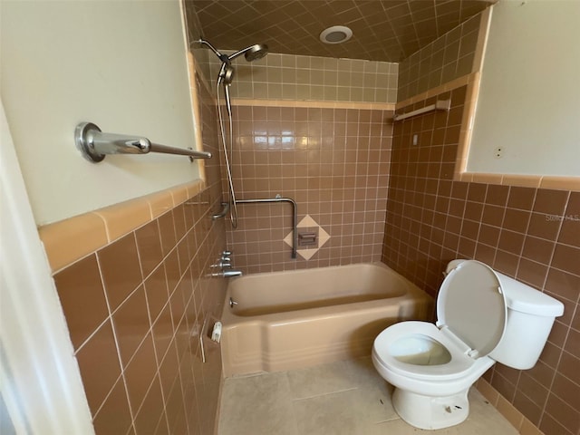 bathroom with toilet, a wainscoted wall, tile patterned flooring, tile walls, and shower / bathing tub combination