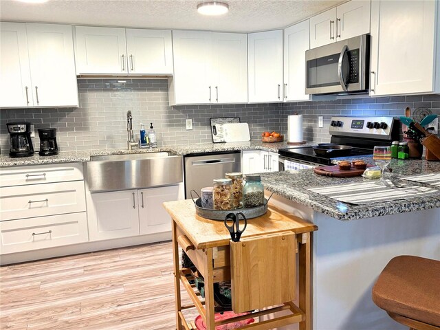 kitchen with appliances with stainless steel finishes, light wood-style floors, white cabinetry, a sink, and a textured ceiling