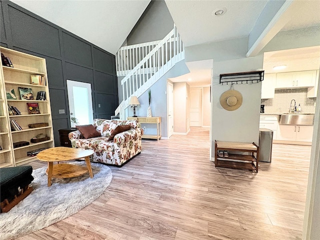 living area featuring high vaulted ceiling, stairs, and light wood-style floors