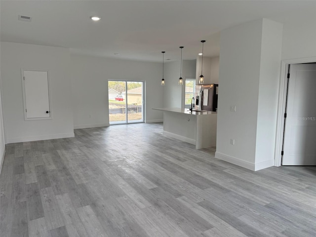 unfurnished living room featuring recessed lighting, baseboards, a sink, and light wood finished floors