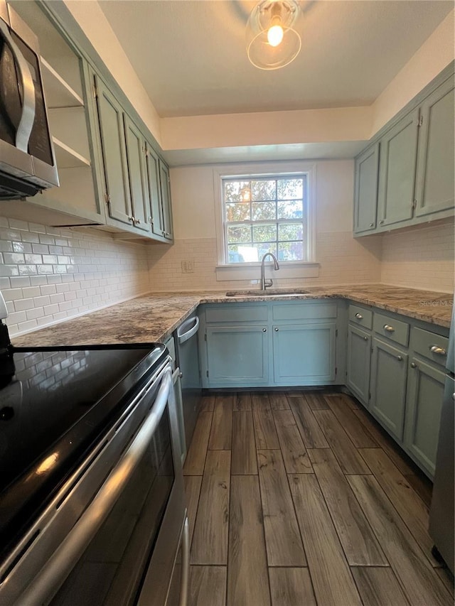 kitchen with decorative backsplash, appliances with stainless steel finishes, light stone counters, dark wood-type flooring, and a sink