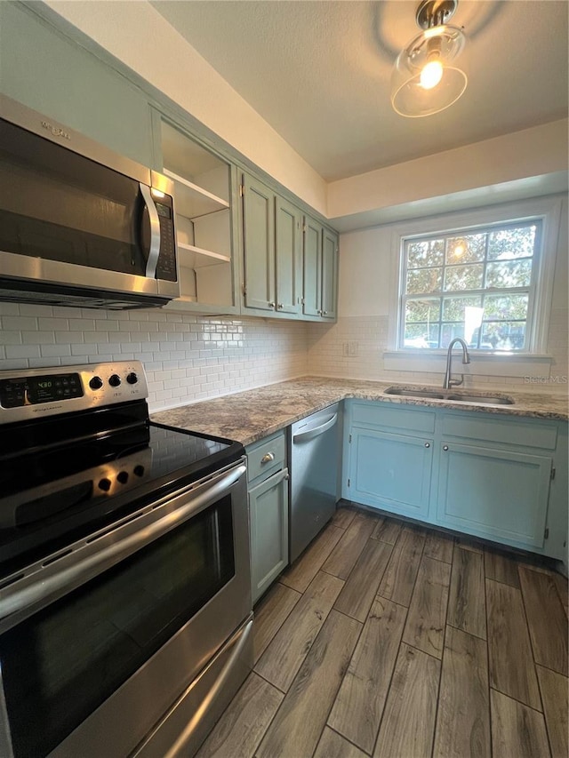 kitchen with wood finished floors, appliances with stainless steel finishes, a sink, and decorative backsplash