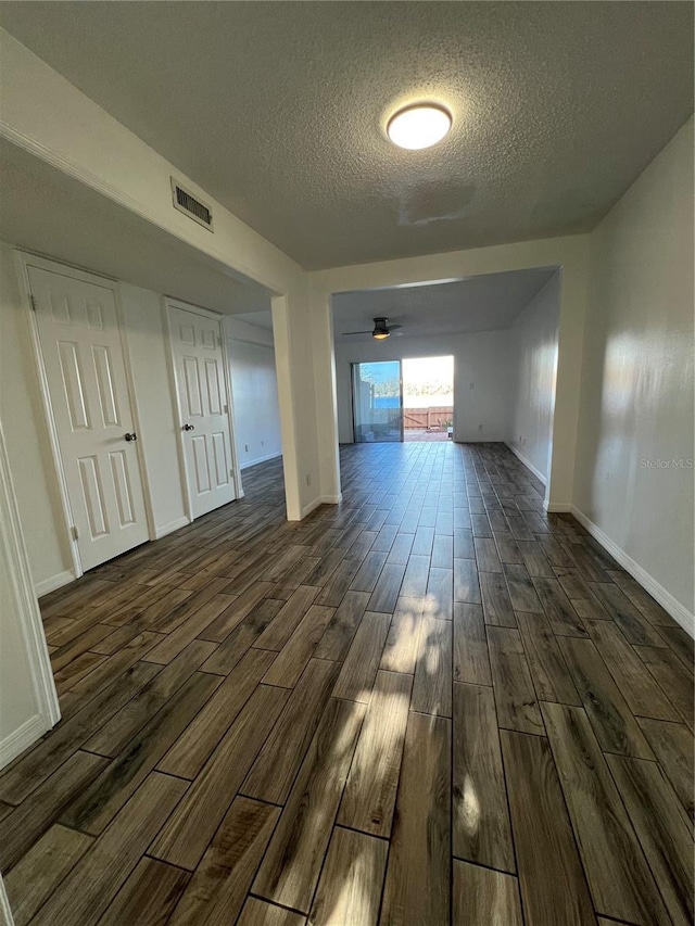 hall featuring dark wood-style floors, visible vents, a textured ceiling, and baseboards