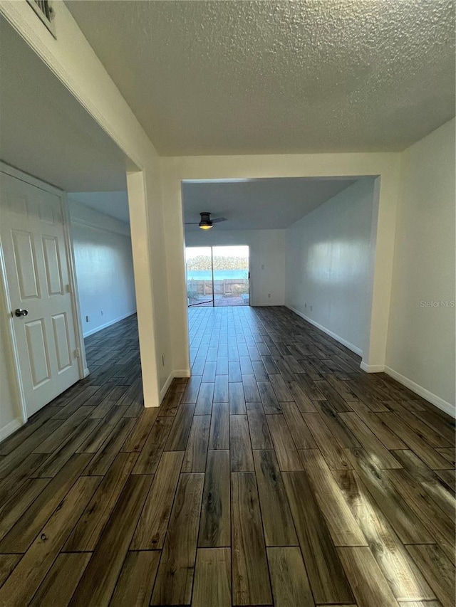 empty room with a textured ceiling, ceiling fan, dark wood-style flooring, visible vents, and baseboards