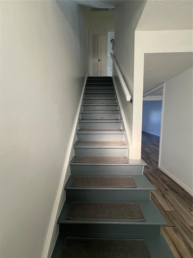 staircase featuring baseboards, a textured ceiling, visible vents, and wood finished floors