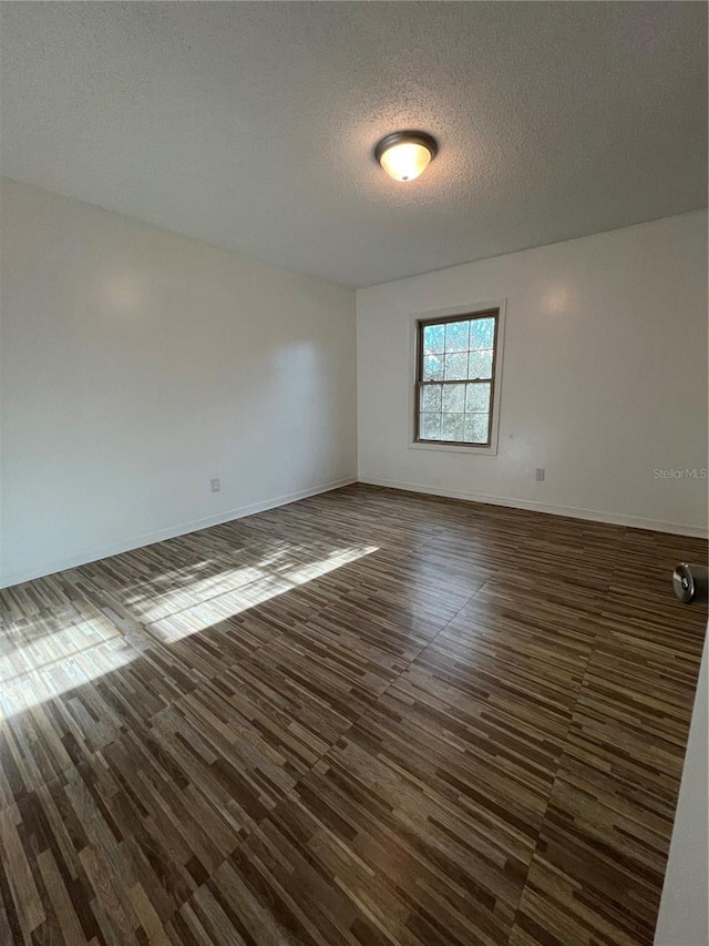 empty room with dark wood-type flooring, a textured ceiling, and baseboards