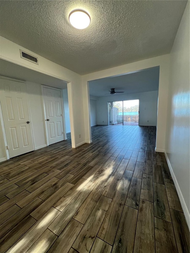 interior space with a textured ceiling, a ceiling fan, visible vents, baseboards, and dark wood-style floors