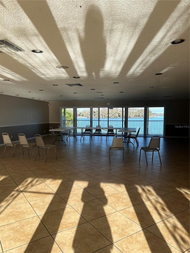 interior space with visible vents, a water view, a textured ceiling, and light tile patterned floors