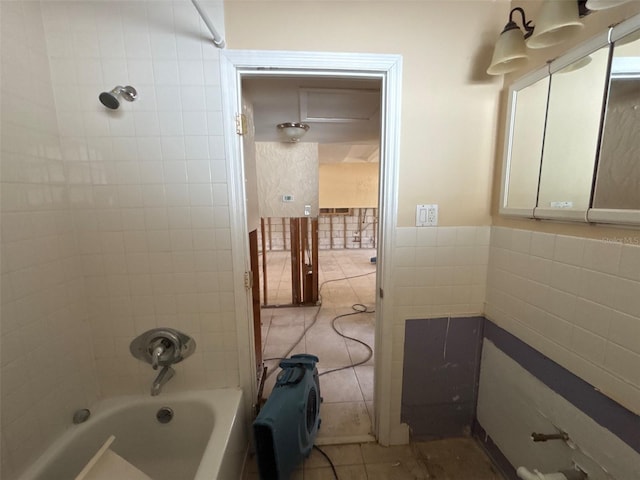 bathroom with a wainscoted wall, tub / shower combination, tile patterned flooring, and tile walls