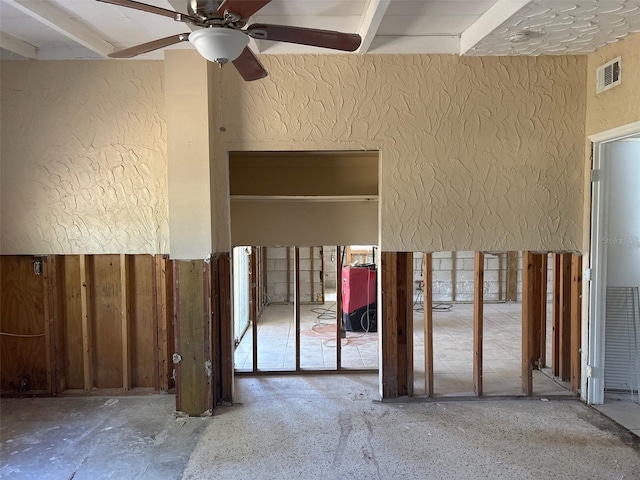 miscellaneous room with visible vents, beamed ceiling, a ceiling fan, and a textured wall