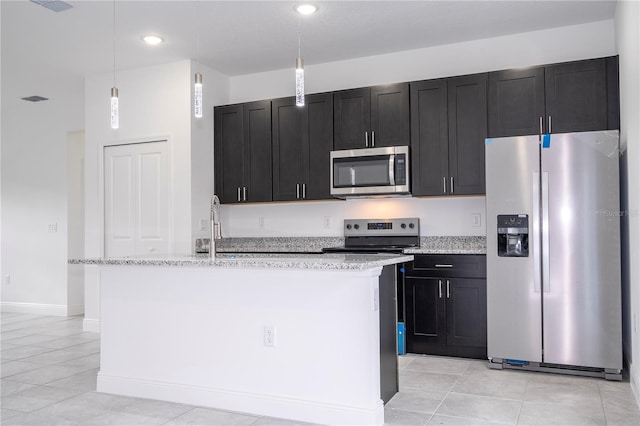 kitchen featuring a kitchen island with sink, a sink, stainless steel appliances, light tile patterned floors, and dark cabinets