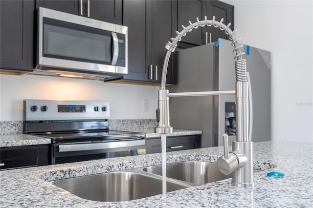 kitchen with light stone countertops, appliances with stainless steel finishes, and dark cabinetry