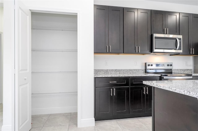 kitchen featuring stainless steel appliances, light tile patterned floors, baseboards, dark cabinets, and light stone countertops