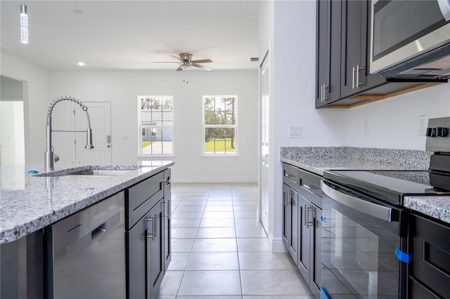 kitchen with light stone countertops, light tile patterned flooring, stainless steel appliances, a ceiling fan, and a sink