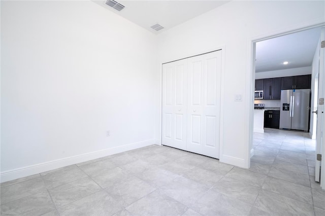 unfurnished bedroom with a closet, visible vents, baseboards, and stainless steel fridge with ice dispenser