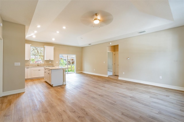 kitchen featuring a center island, a raised ceiling, light wood-style flooring, open floor plan, and white cabinetry