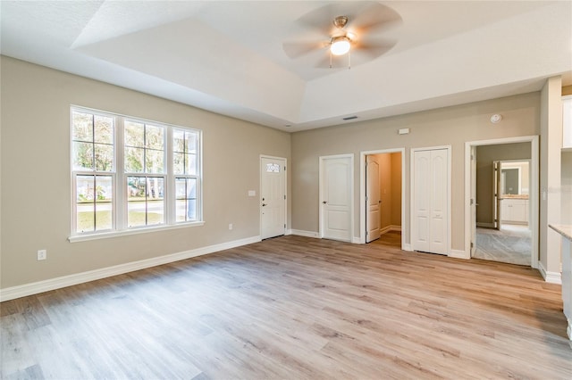 unfurnished bedroom featuring a raised ceiling, light wood-style flooring, and baseboards