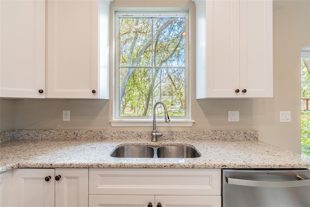 kitchen with light stone counters, stainless steel dishwasher, a sink, and white cabinetry