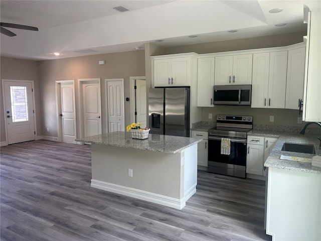 kitchen with visible vents, appliances with stainless steel finishes, white cabinets, a kitchen island, and a sink