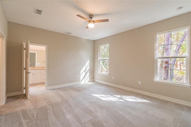 spare room with light carpet, ceiling fan, visible vents, and baseboards