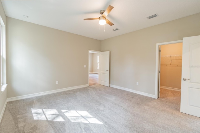 unfurnished bedroom featuring a walk in closet, a closet, light carpet, and baseboards