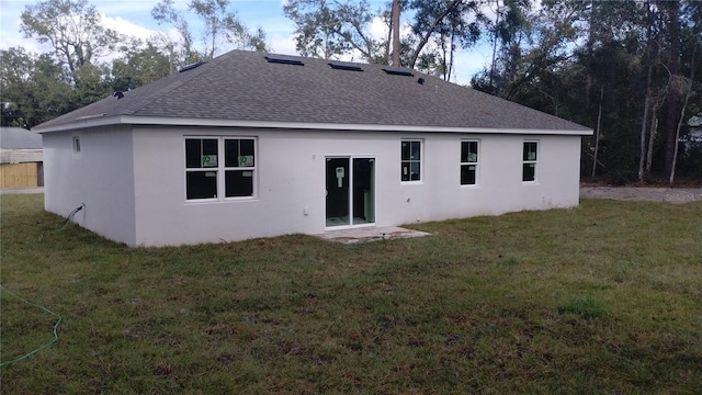 rear view of house with stucco siding, roof with shingles, and a yard