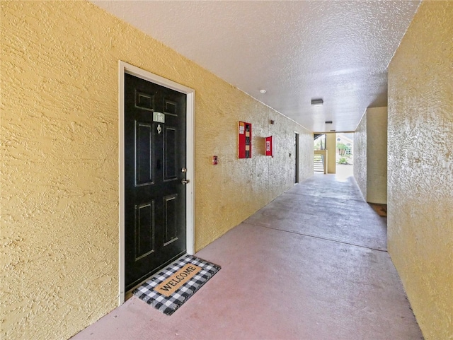 hallway featuring concrete floors, a textured ceiling, and a textured wall