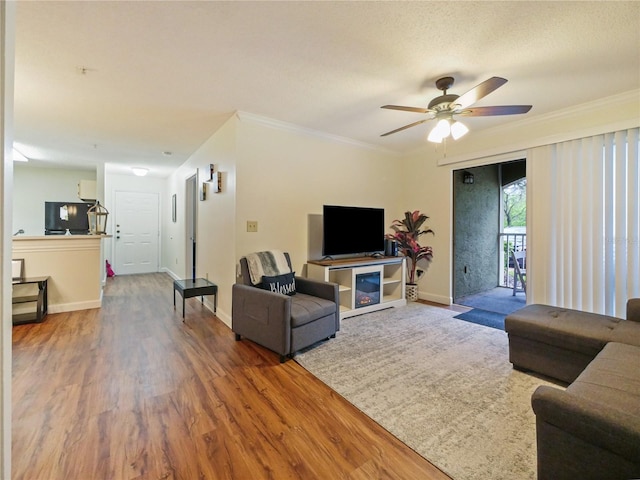 living room featuring baseboards, ceiling fan, wood finished floors, and crown molding