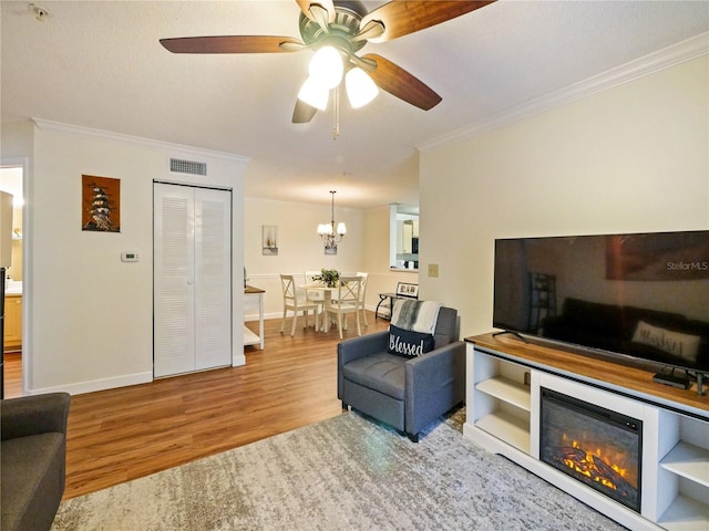 living room with crown molding, visible vents, a glass covered fireplace, wood finished floors, and baseboards