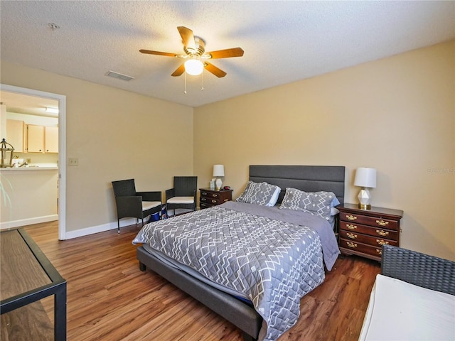 bedroom featuring visible vents, baseboards, a ceiling fan, wood finished floors, and a textured ceiling