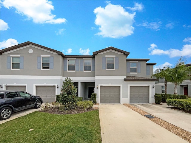 view of property featuring a garage, driveway, a front lawn, and stucco siding