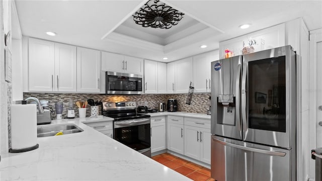 kitchen featuring appliances with stainless steel finishes, a tray ceiling, white cabinets, and backsplash